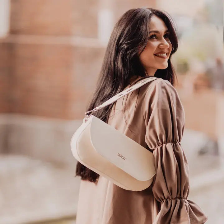 Woman carrying a cream colored bag with a blurred background .plant based ivory leather bad made from apple peels.  Classic shoulder bag with fold-over design