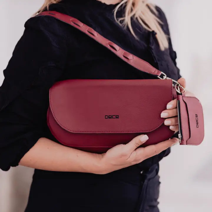 Person holding a red handbag on a plain background. plant based garnet colored leather bad made from apple peels.  Classic shoulder bag with fold-over design