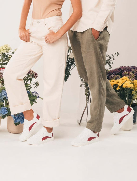 Two people wearing white sneakers with red accents standing in front of floral arrangements.