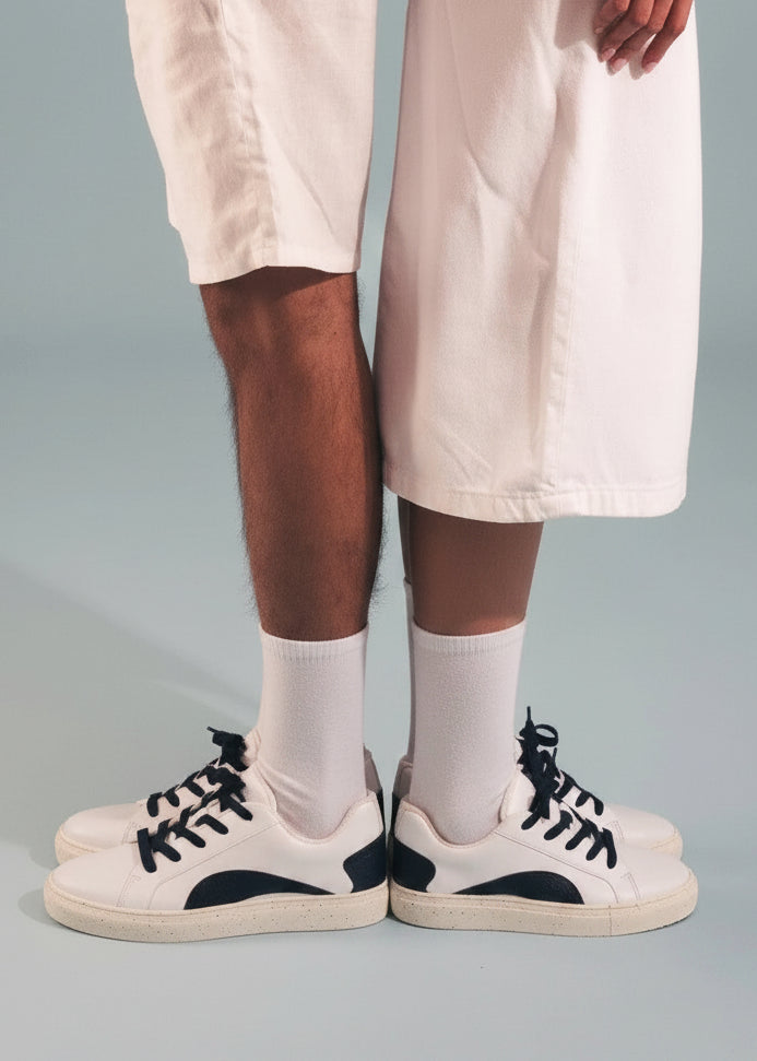 Person wearing white sneakers with black accents, beige shorts, and socks with on a gray background.